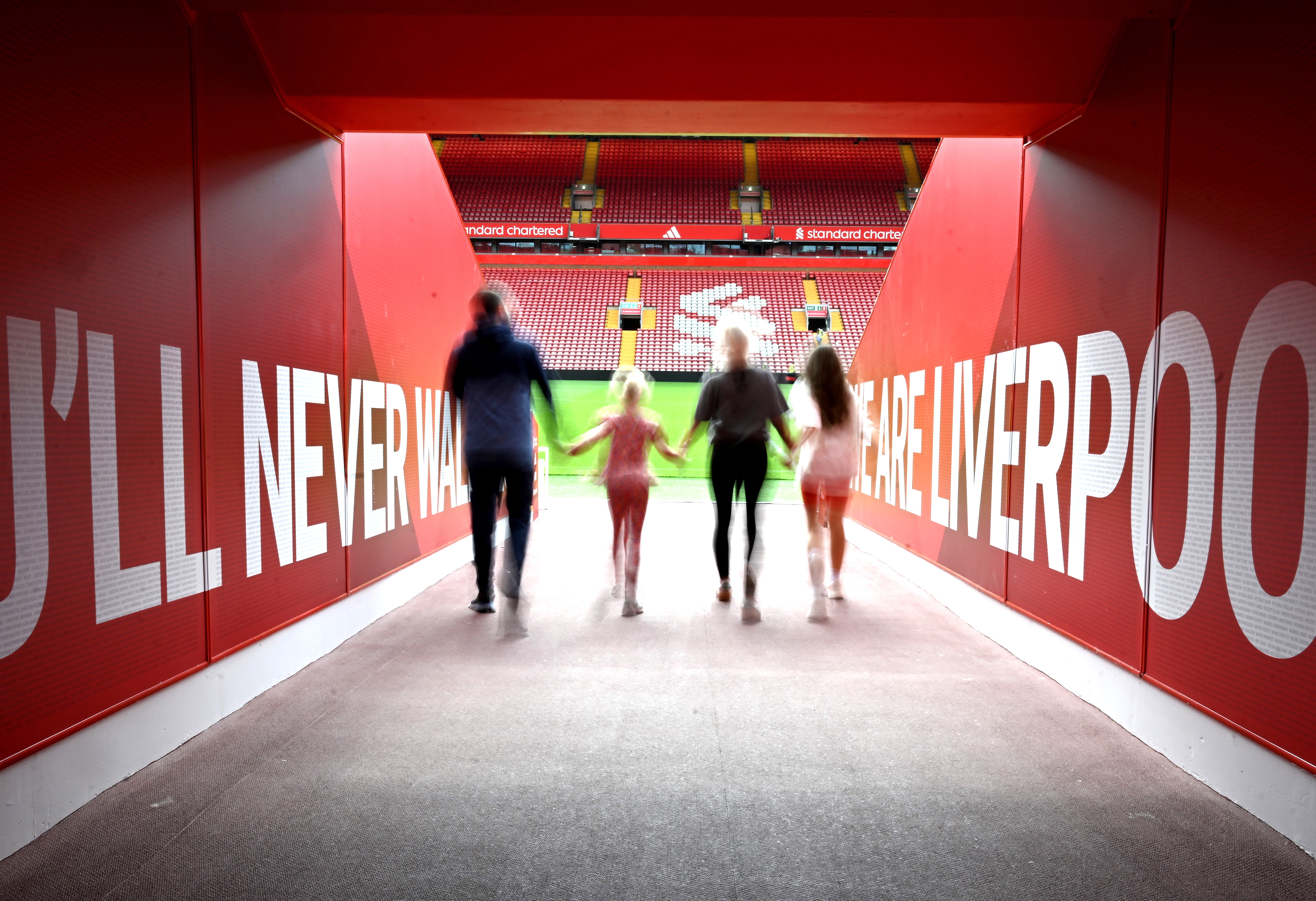 Man posing for photograph touching This is Anfield sign in the tunnel and man taking his photo